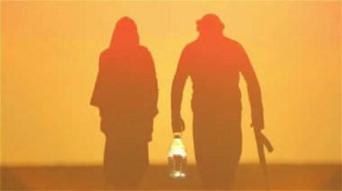 Günbatımında silahlı Arap mülteciler. Çöldeki Müslüman çift, ellerinde silah ve bir şişe suyla.. 