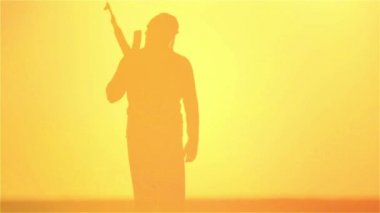 Günbatımında Kalaşnikof ile İslam savaşçısı. Müslüman savaşçı gün batımında makineli tüfekle antrenman yapıyor.. 