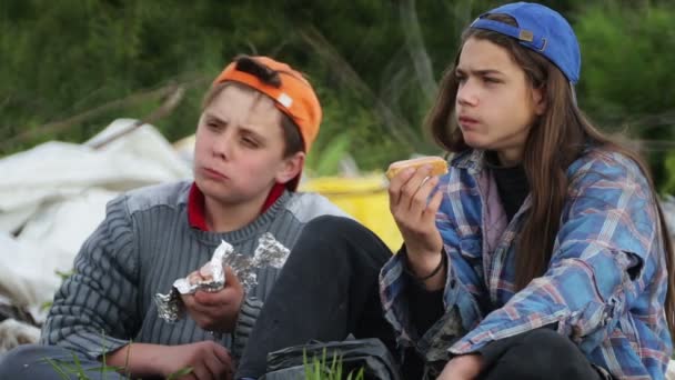 ホームレスの子供たちは埋め立て地で食べ物を食べる 二十代のお尻食べるサンドイッチで発見されたゴミ箱 — ストック動画