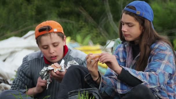 无家可归的儿童在垃圾填埋场里吃食物 两个年轻人在吃垃圾里发现的三明治 — 图库视频影像