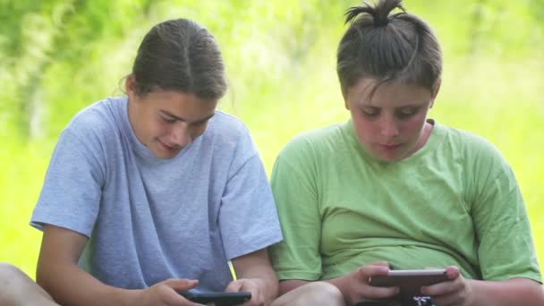 10代の少年たちは公園のスマートフォンで遊んでいる 子供たちはインターネット上で携帯電話でゲームをプレイ — ストック動画