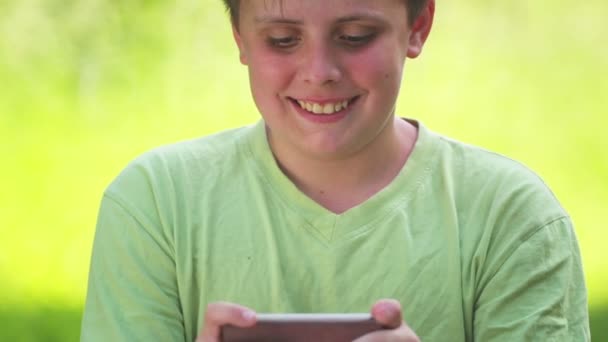 男の子はスマートフォンでゲームをする 赤ちゃん男の子ティーネージャーは公園でネット上でゲームをプレイ — ストック動画