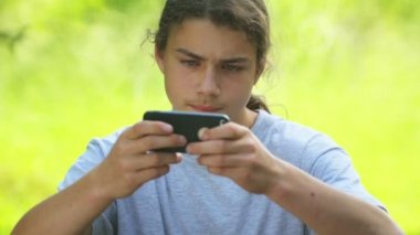 Bir çocuk akıllı telefondan oyun oynuyor. Küçük oğlan parkta internette bir oyun oynuyor..  