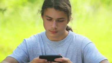 Bir çocuk akıllı telefondan oyun oynuyor. Küçük oğlan parkta internette bir oyun oynuyor..  