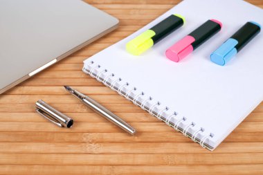Ahşap arka plan üzerinde laptop, işaretçileri, defter ve DIP kalem ile çalışma alanının Üstten Görünüm.