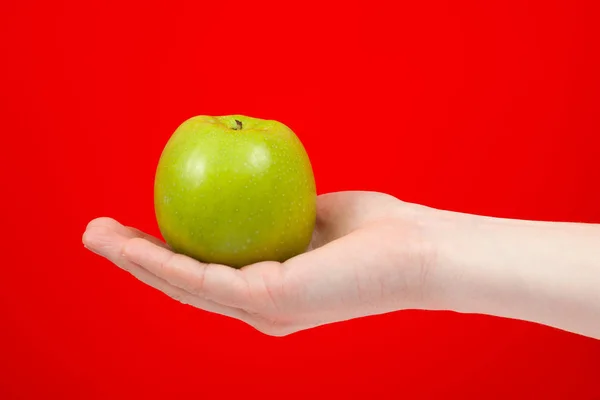 Χέρι κρατώντας νόστιμο βιολογικό πράσινο νόστιμο μήλο απομονωμένη στο κόκκινο — Φωτογραφία Αρχείου