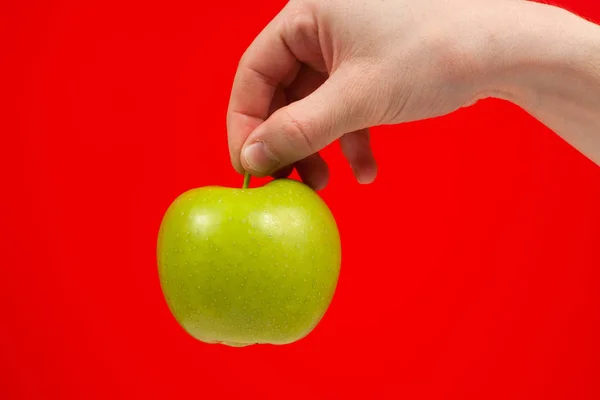 Рука тримає смачне зелене смачне яблуко Ізольовані на червоному — стокове фото
