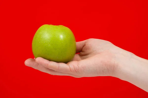 Ręka trzyma smaczne organiczne zielone pyszne jabłko izolowane na czerwono — Zdjęcie stockowe