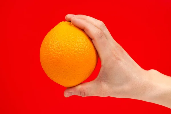 Reife saftige köstliche Orange in der Hand isoliert auf rotem Hintergrund. — Stockfoto