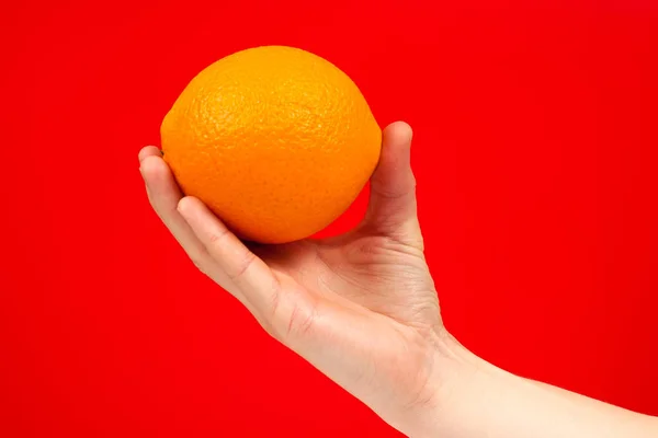 Reife saftige köstliche Orange in der Hand isoliert auf rotem Hintergrund. — Stockfoto