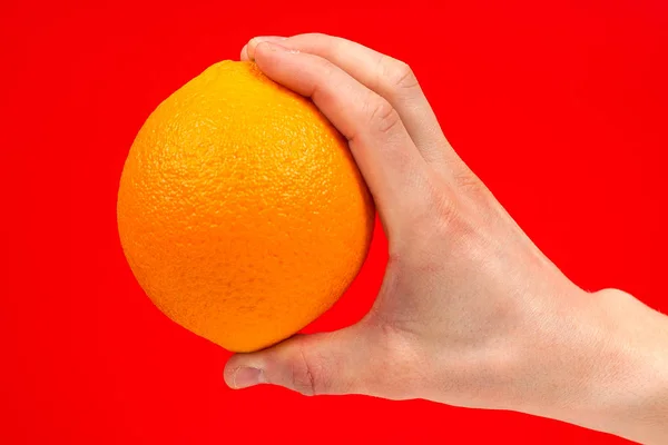 Reife saftige köstliche Orange in der Hand isoliert auf rotem Hintergrund. — Stockfoto