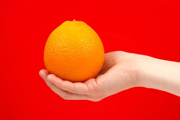 Reife saftige köstliche Orange in der Hand isoliert auf rotem Hintergrund. — Stockfoto