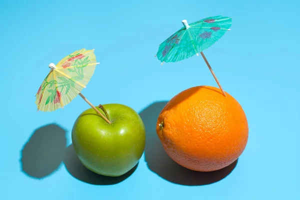 Fresh juicy orange and green apple with a cocktail umbrella isol