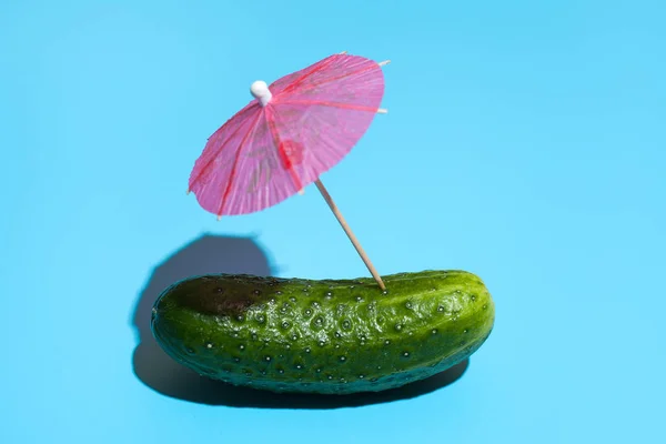 Fresh cucumber with a cocktail umbrella isolated on blue backgro