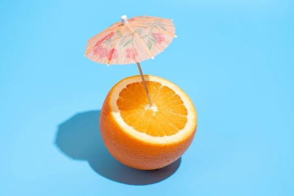 Fresh juicy orange with a cocktail umbrella isolated on blue bac