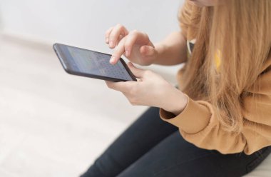 Ofiste boş ekranlı, elinde siyah cep telefonu olan bir kadının ellerinin görüntüsü.