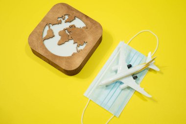 Uçak modeli, yüz maskesi ve sarı arka planda toprak modeli. Coronavirüs 'ün uçuş etkisi (COVID-19) kavramı.