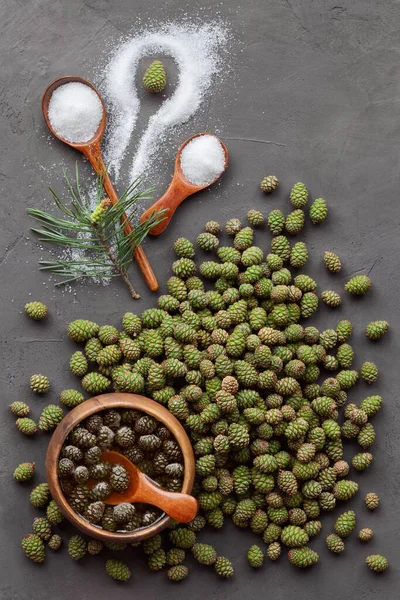 Young pine cones and jam on a dark background. Green cones, sugar and jam in a wooden bowl. Harvest from the forest