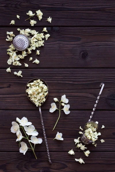 Dried jasmine flowers for tea and retro tea strainers on a dark wooden background. Composition of fresh and dried jasmine flowers with copy space for text. Making aromatic tea. Top view.