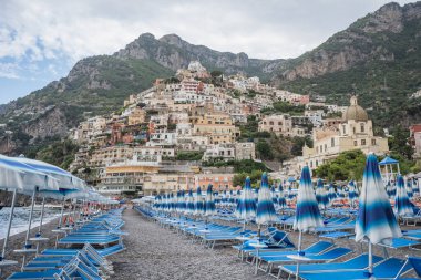 Arka planda Amalfi kayalıkları olan şemsiye yataklı Positano plajı.