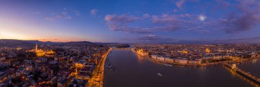 Budapeşte 'de kış günü günbatımında Tuna Nehri' nin mor gökyüzü ile aydınlanmış panoramik drone görüntüsü.