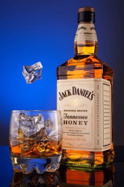 Viski şişe Jack Deniels bal ve bir bardak buz cam ve mavi bir arka plan ile.