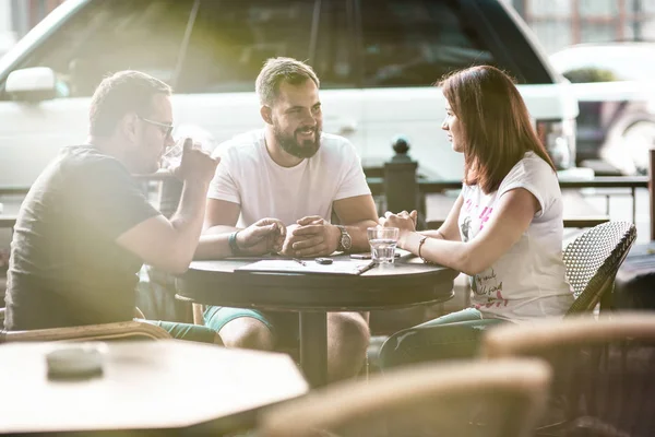 Side view and top. The company of three businessmen are discussing at the table in coffee, writing in a notebook, looking at a laptop, satkan with water, car keys, magazines, a smartphone, online transactions.