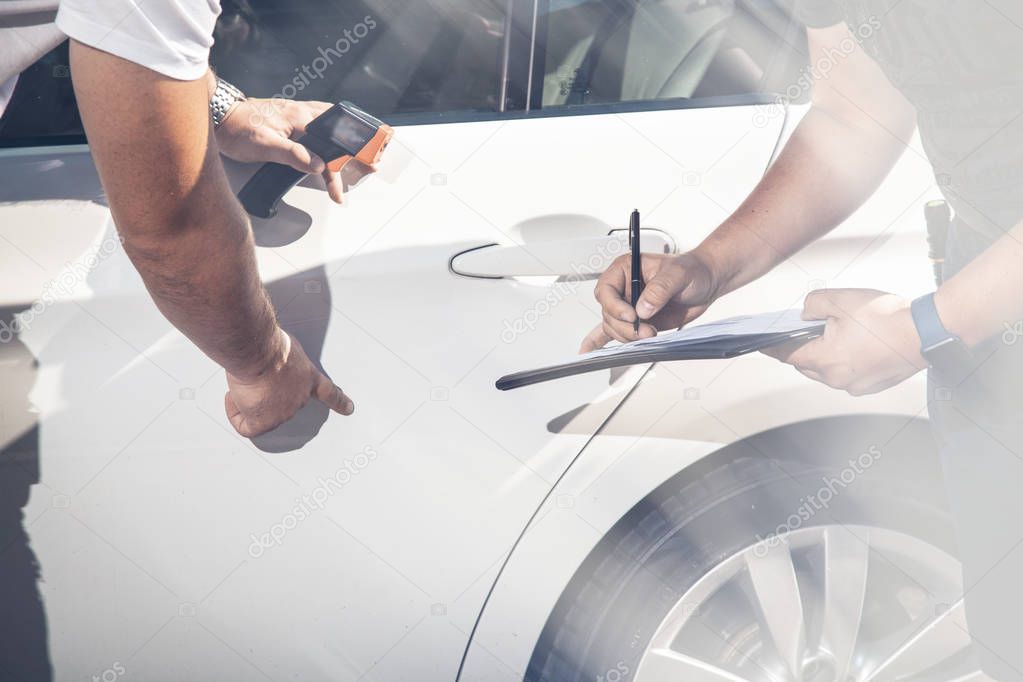 Against the background of a white car, inspectors inspect the transport vehicle, record defects.