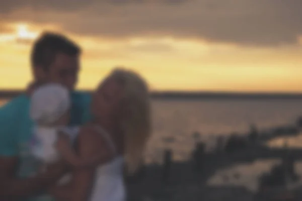 Blurred - young family father mother and daughter at sunset on the lake. — Stock Photo, Image