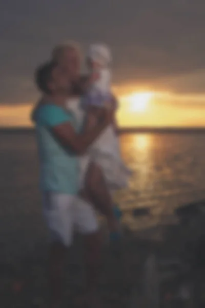 Homályos fiatal család apa-anya és lánya, napnyugtakor a tavon. — Stock Fotó