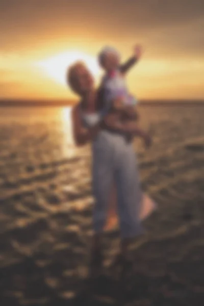 Wazig - jonge moeder en haar dochter bij zonsondergang op het meer. — Stockfoto