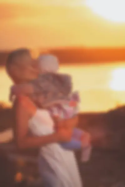 Sfocato - Giovane madre e sua figlia al tramonto sul lago . — Foto Stock