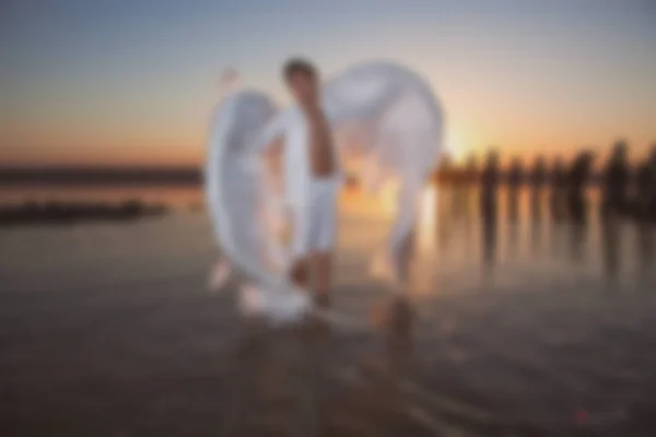 Wazige foto voor achtergrond, Angel bij zonsondergang aan zee, goed idee fantasie. — Stockfoto