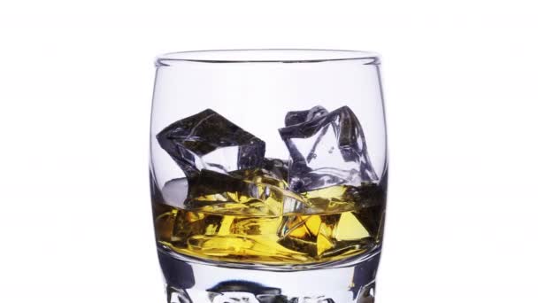 ウイスキーとアイスキューブが白の上にストップモーションズーム効果で充填し 空にするガラス — ストック動画