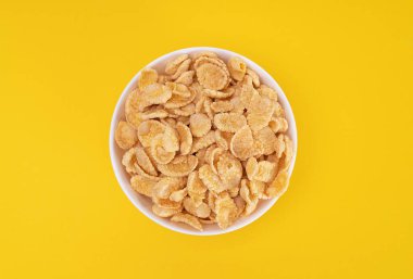 Sarı arka planda lezzetli bir kahvaltı için mısır gevrekli beyaz tabak. Vitamin açısından zengin sağlıklı yiyecekler..