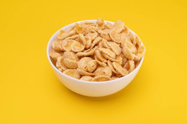 Sarı arka planda lezzetli bir kahvaltı için mısır gevrekli beyaz tabak. Vitamin açısından zengin sağlıklı yiyecekler..