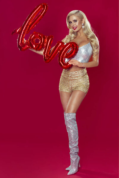 Очаровательная девушка Валентина с длинными светлыми волосами позирует в блестящей одежде, держа в руках надпись любви на воздушном шаре
.