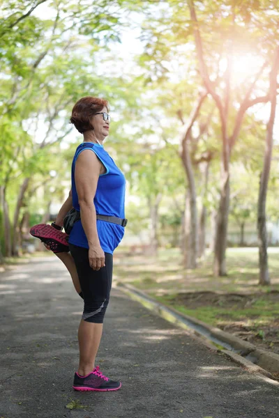 上級アジアの女性は 公園と音楽を聴くことで太ももの筋肉を伸ばします 一緒に運動競技シニア屋外 屋外を実行する前にストレッチ フィットの上級ランナー — ストック写真