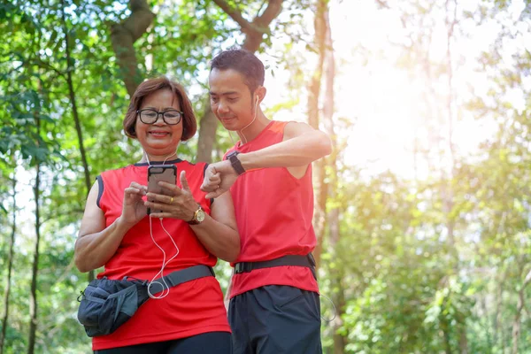 高级亚洲妇女与男子或私人教练检查时间从手机和智能手表 老年护理运动运动概念的心率检查 — 图库照片