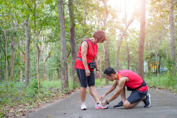 愉快的高级亚洲妇女与人或私人教练系鞋带在公园 老人护理运动活动跑步者准备慢跑概念 — 图库照片