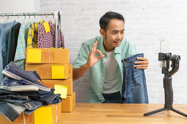 Азіатський людина показані добре і за допомогою смарт-мобільний телефон беручи жити продажу брюки джинси онлайн, запис рішень відео Blogger камера запуск малого бізнесу власник — стокове фото