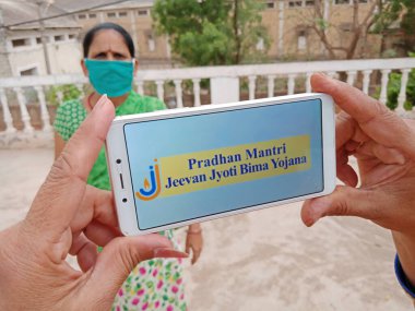 Katni Bölgesi, Madhya Pradesh, Hindistan - 23 Mayıs 2020: pradhan mantri jeevan jyoti bima yojana hükümet planı açık arkaplanda Hintli bir kadın tarafından akıllı telefon ekranında gösterildi.