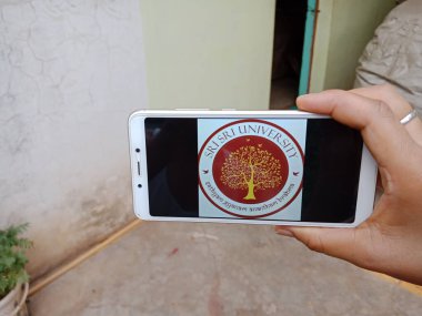 DISTRICT KATNI, INDIA - 28 Mayıs 2020: Shri Shri üniversite logosunu ekranda gösteren akıllı telefon tutan Hintli bir kadın, köylüler için modern eğitim kavramı.