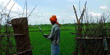 DİSTRİK KATNI, INDIA - 14 AĞUSTOS 2019: Bir Hintli köylü erkek çiftçi yeşil tarla etrafında dizüstü bilgisayar kullanıyor.