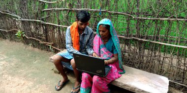 DİSTRİK KATNI, INDIA - 14 Ağustos 2019: Hindistan köyünden yaşlı bir çiftçi kadın, torunuyla birlikte tarım yeşil tarlaları etrafında dizüstü bilgisayar teknolojisini öğreniyor.