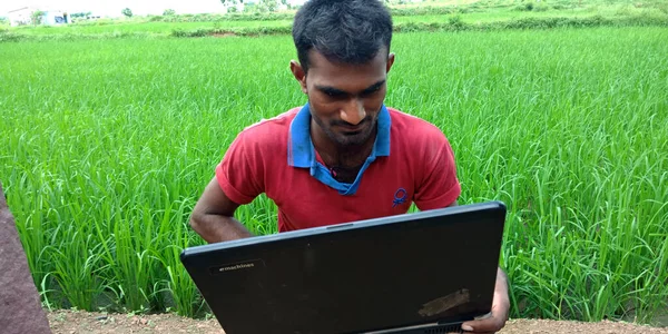 DİSTRİK KATNI, INDIA - 14 AĞUSTOS 2019: Tarım yeşil alanı etrafında dizüstü bilgisayar kullanan Hintli bir köy çocuğu.