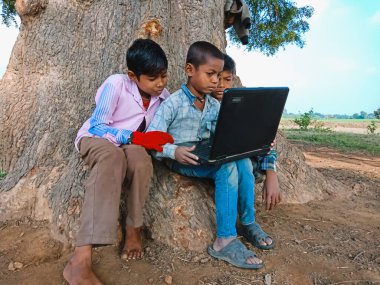 DİSTRİK KATNI, INDIA - HAZİRAN 01, 2020: Ağacın yakınındaki açık alanda arkadaşlarına dizüstü bilgisayar teknolojisini öğreten Hintli bir çocuk.