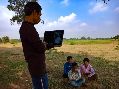 DISTRICT KATNI, INDIA - HAZİRAN 01, 2020: Açık alandaki fakir çocuklara dizüstü bilgisayar teknolojisi hakkında eğitim veren Hintli bir şehir çocuğu.