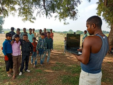 DISTRICT KATNI, INDIA - HAZİRAN 01, 2020: Bir Hintli köylü açık alandaki fakir çocuklara dizüstü bilgisayar teknolojisi hakkında eğitim veriyor.