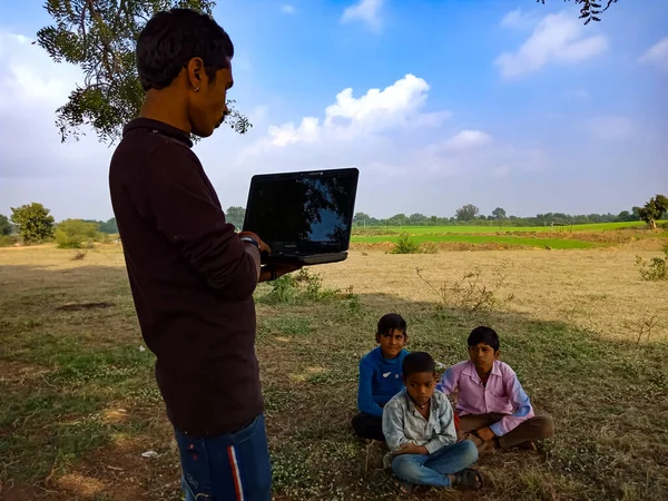 DISTRICT KATNI, INDIA - HAZİRAN 01, 2020: Açık alandaki fakir çocuklara dizüstü bilgisayar teknolojisi hakkında eğitim veren Hintli bir şehir çocuğu.